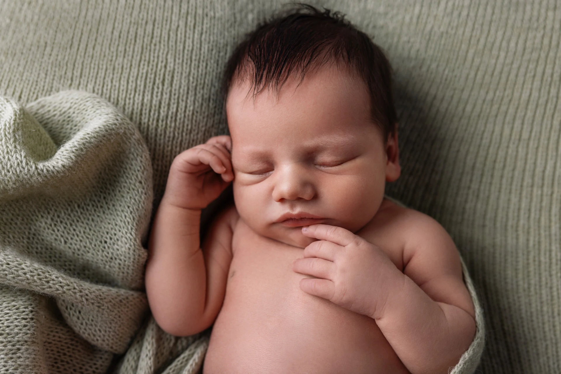 Primo piano di neonato addormentato su coperta verde con la manina vicino al volto, servizio newborn a Bologna