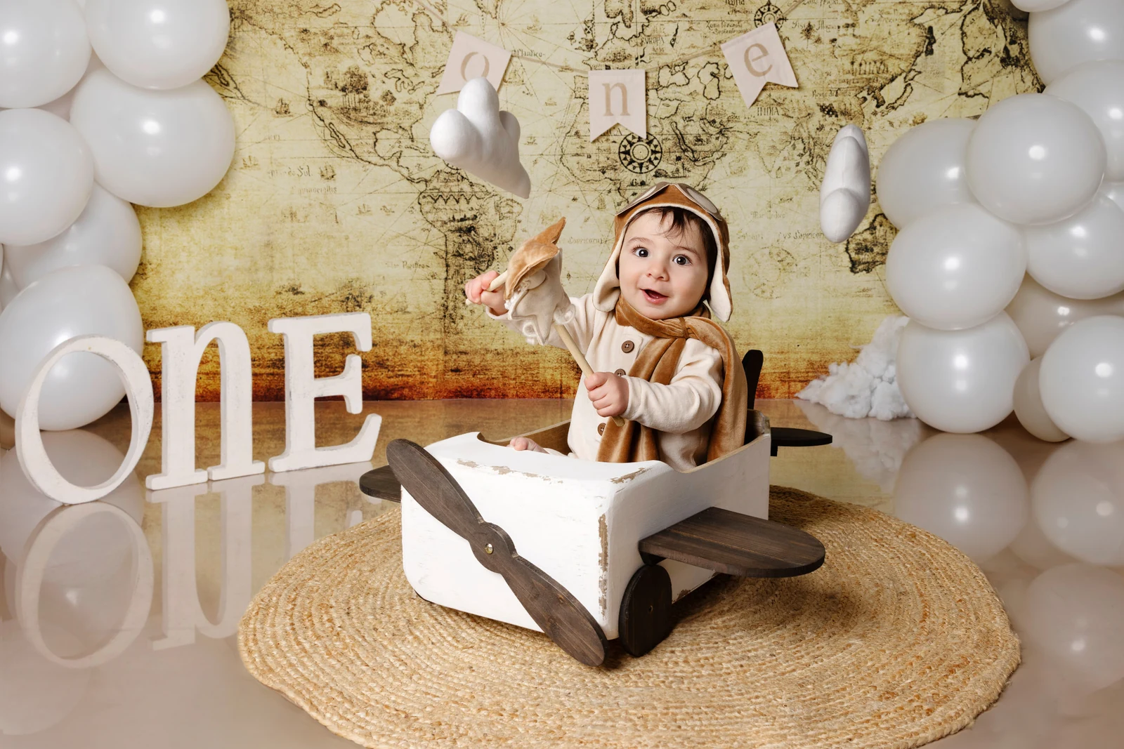Bambino aviatore seduto nell'aeroplanino di legno con un giocattolo — fondale mappa e lettere "ONE", smash cake primo compleanno a Bologna.