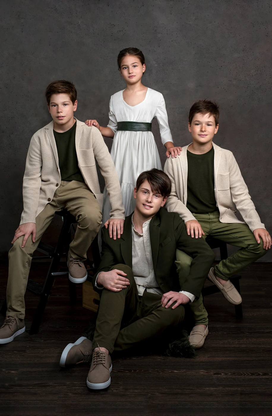 Ritratto fine art di quattro fratelli in abiti eleganti verde oliva e beige, composizione simmetrica su sfondo scuro — fotografia di famiglia a Bologna.