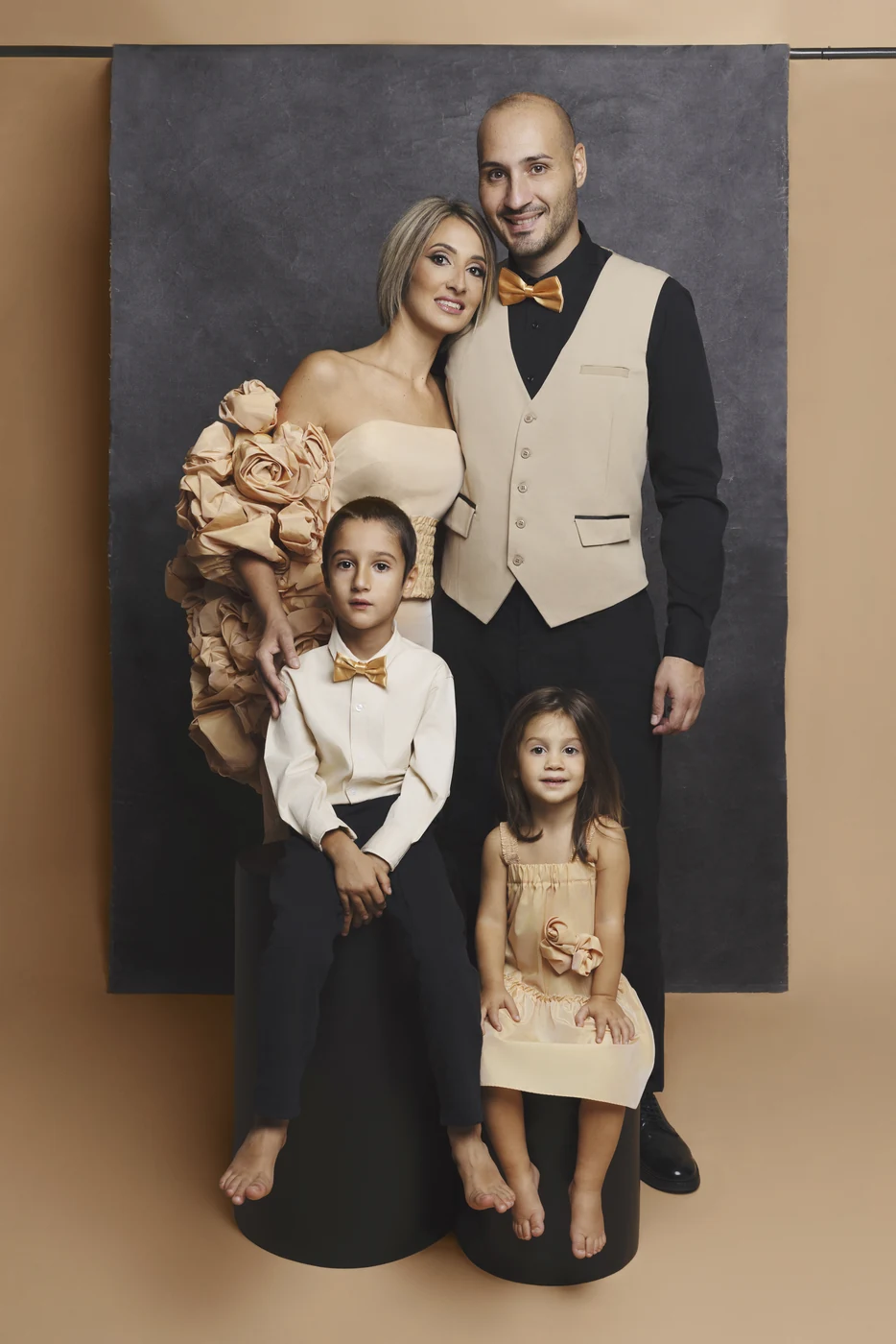 Ritratto di famiglia fine art a Bologna: genitori con un bambino e una bambina in eleganti toni cipria e oro su fondale grigio.