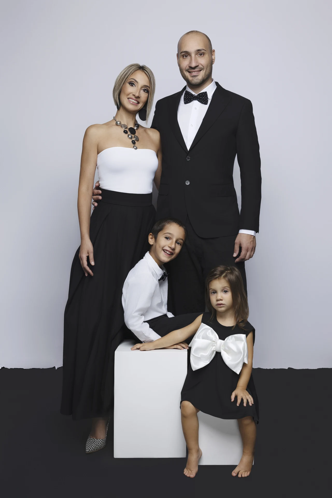 Ritratto di famiglia in bianco e nero a Bologna: genitori e due bambini in abiti eleganti neri e bianchi su fondale bicolore.