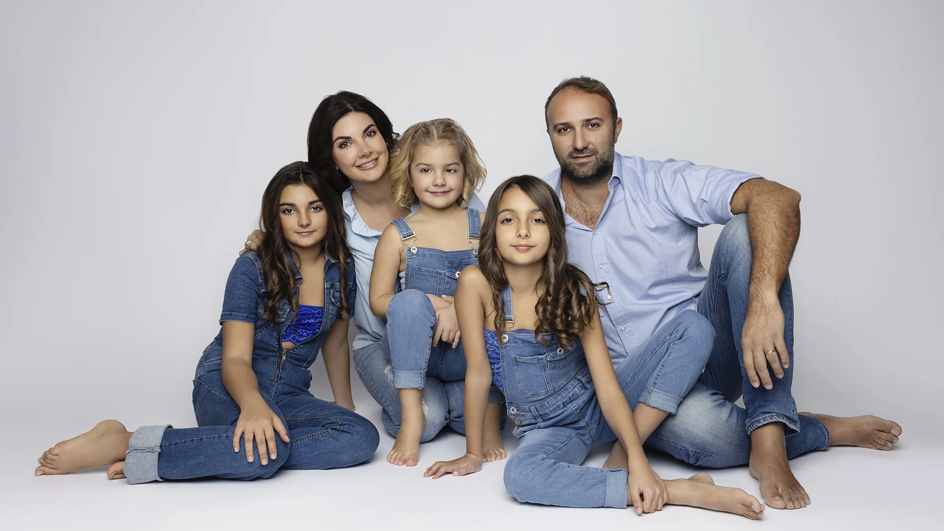 Ritratto di famiglia in studio a Bologna: genitori e tre figlie in denim coordinato su fondo chiaro.