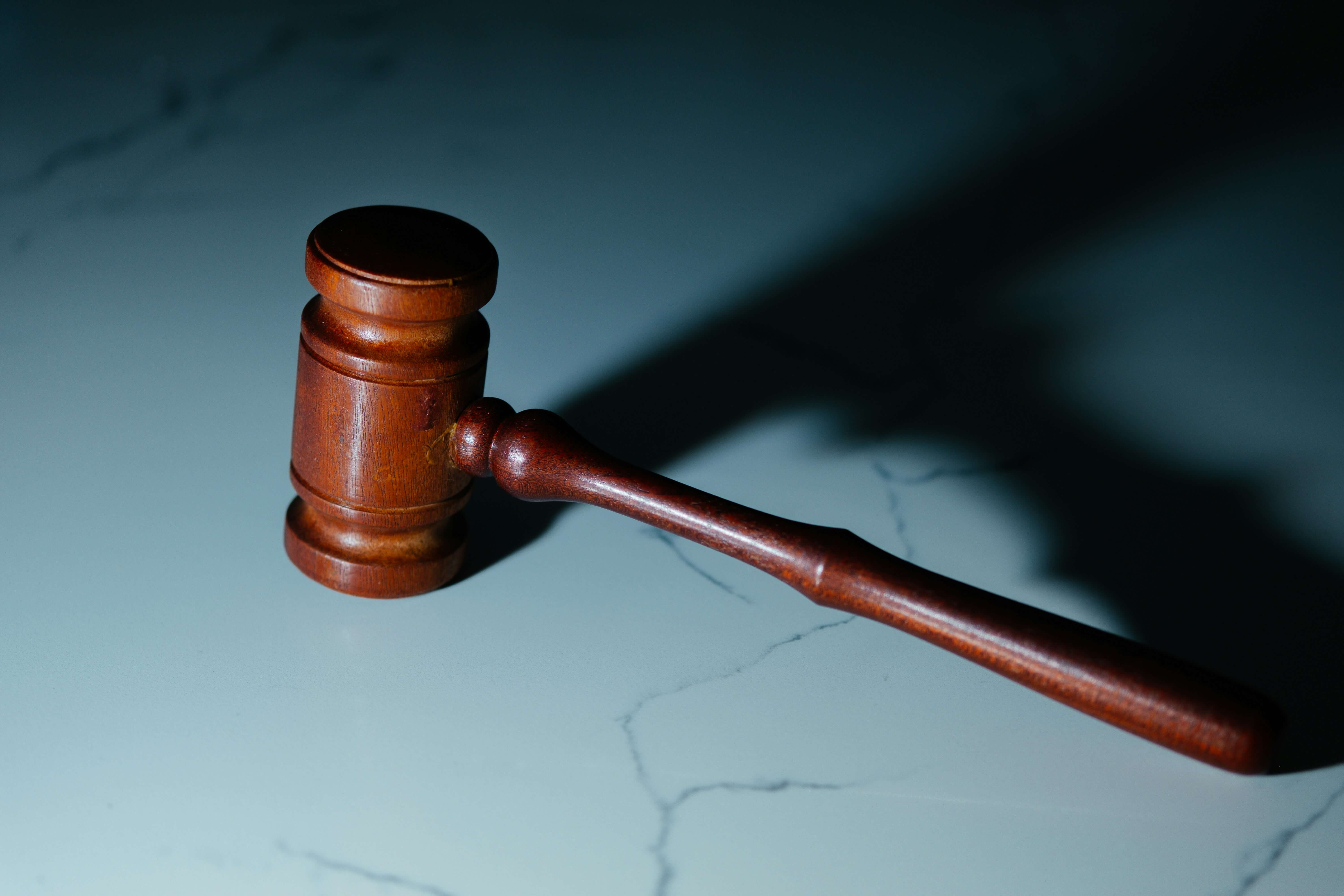 Wooden judge's gavel resting on a marble surface with shadows cast to the right.