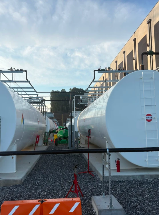 Two large white industrial storage tanks with ladders beside a building under a cloudy sky.