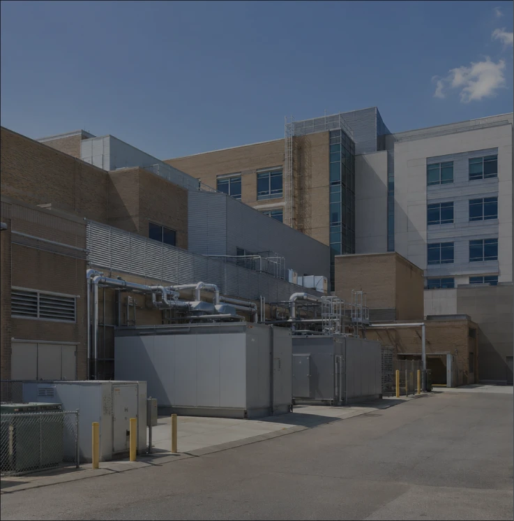 Exterior of an industrial building with ventilation units, pipes, and an alley under clear sky.