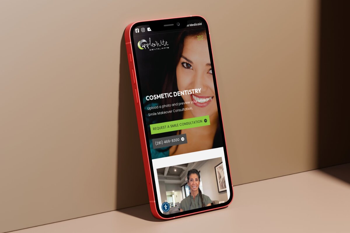 Red smartphone leaning against a beige surface displaying the AppleWhite Dental Arts website with a cosmetic dentistry consultation offer, a smiling woman's face, and a contact number.
