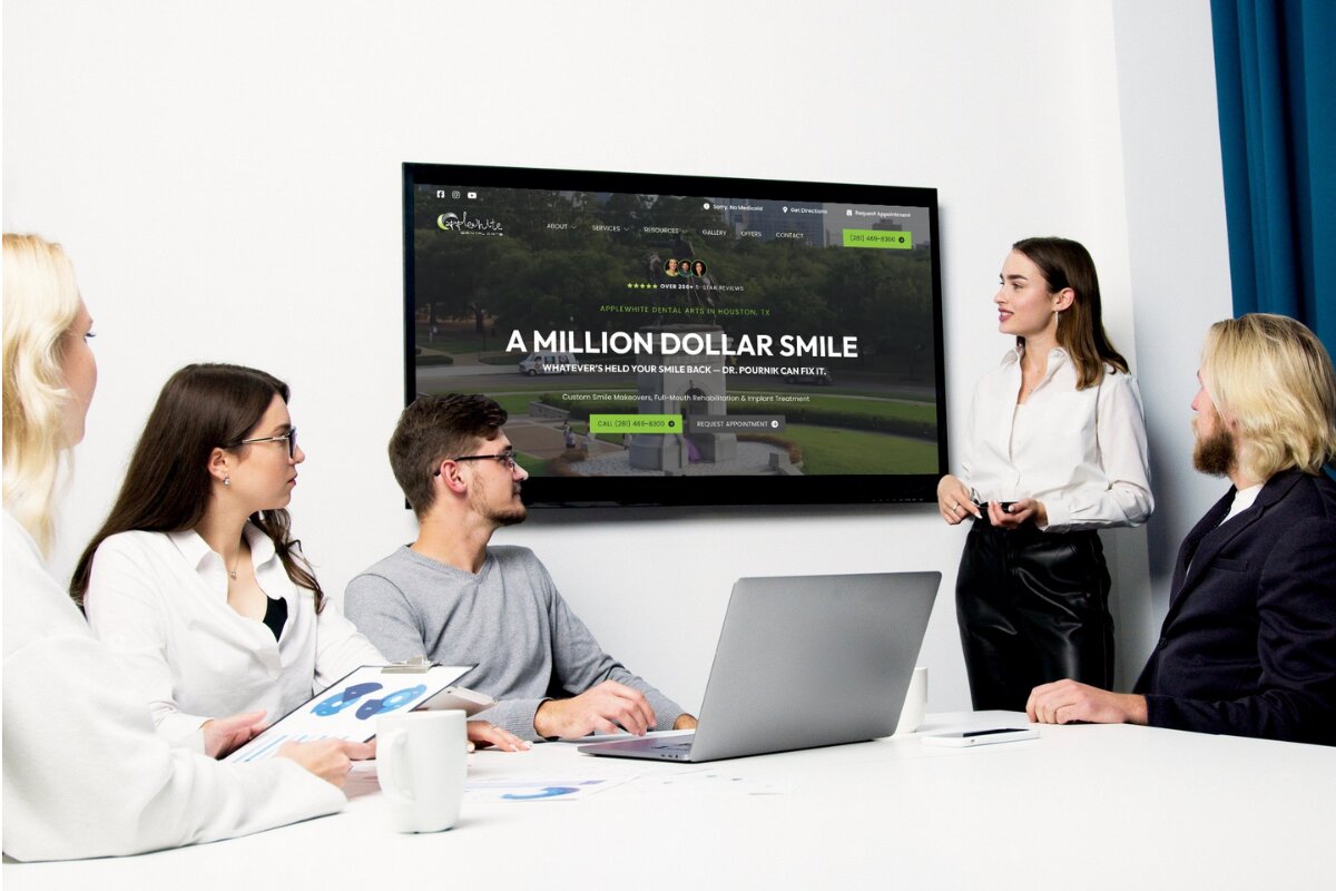 A group of five people in a meeting room, with a woman in a white blouse standing and presenting information displayed on a wall-mounted screen behind her, showing the homepage of Applewhite Dental Arts in Houston, TX, promoting dental services with a headline 'A Million Dollar Smile'.