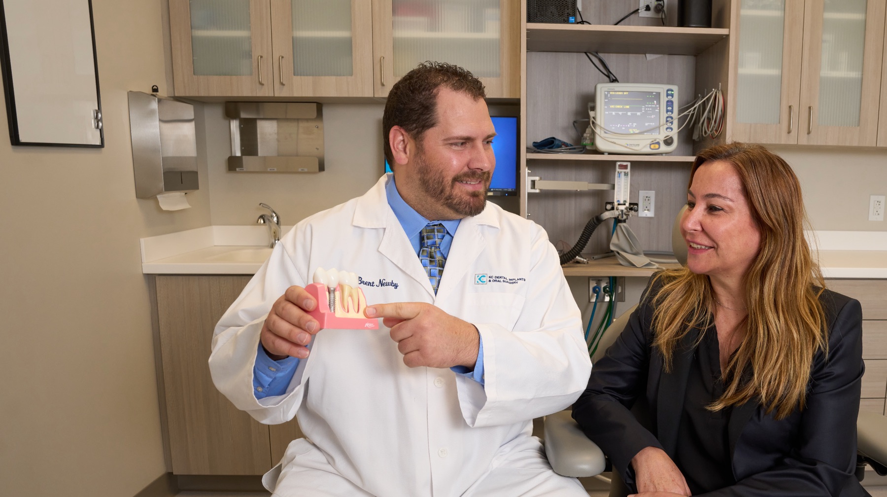 A dentist shows a patient an implant teeth model.