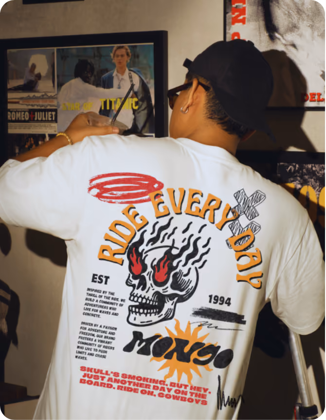 Person wearing a white t-shirt with a graphic on the back showing a flaming skull with red eyes, surrounded by text that reads 'RIDE EVERY DAY,' 'EST 1994,' 'MONGO,' and additional smaller text about adventure and freedom.