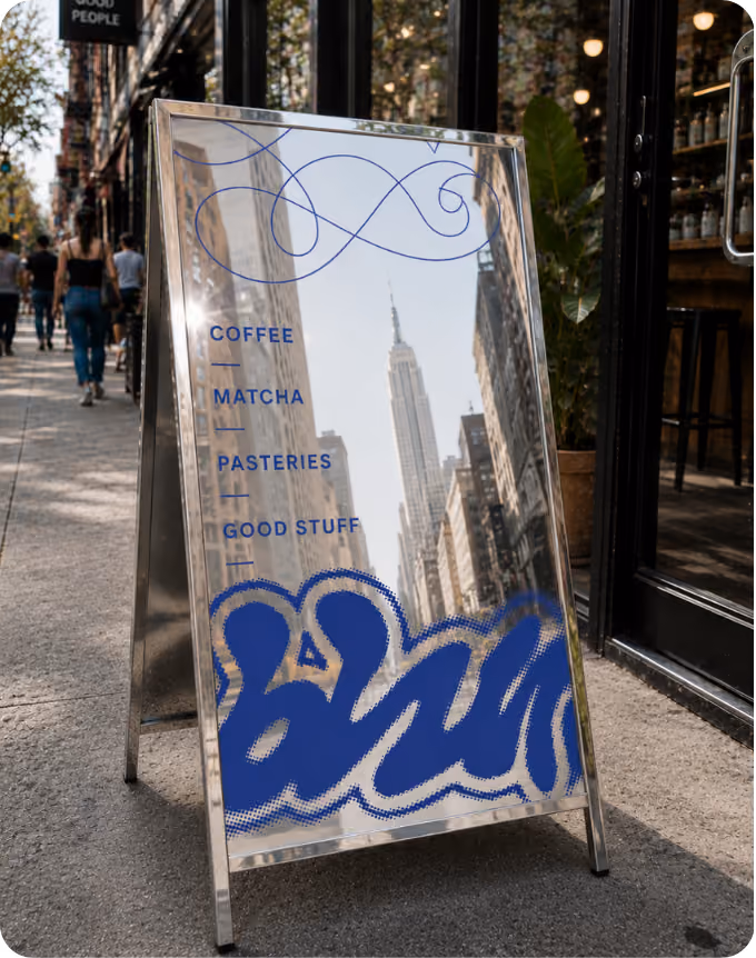 Metal sandwich board outside a cafe reflecting city buildings including the Empire State Building, with text listing coffee, matcha, pastries, and good stuff.