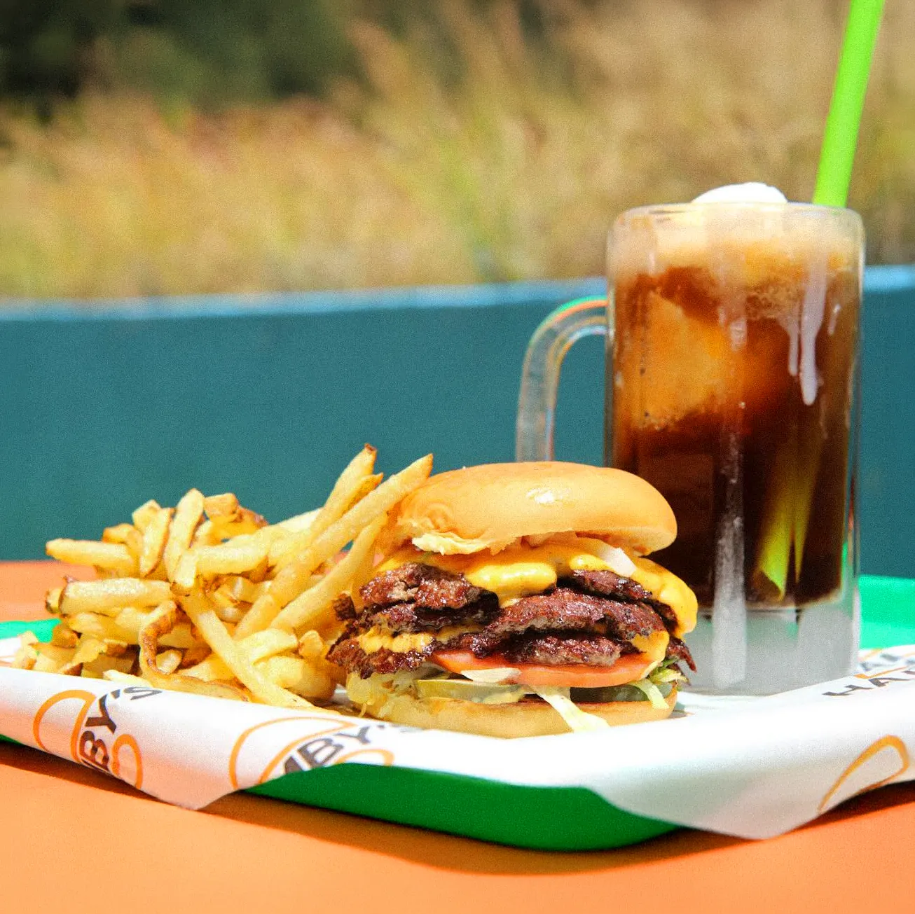 A cheeseburger rests on Hamby's printed paper with fries and a frosty root beer float beside it.