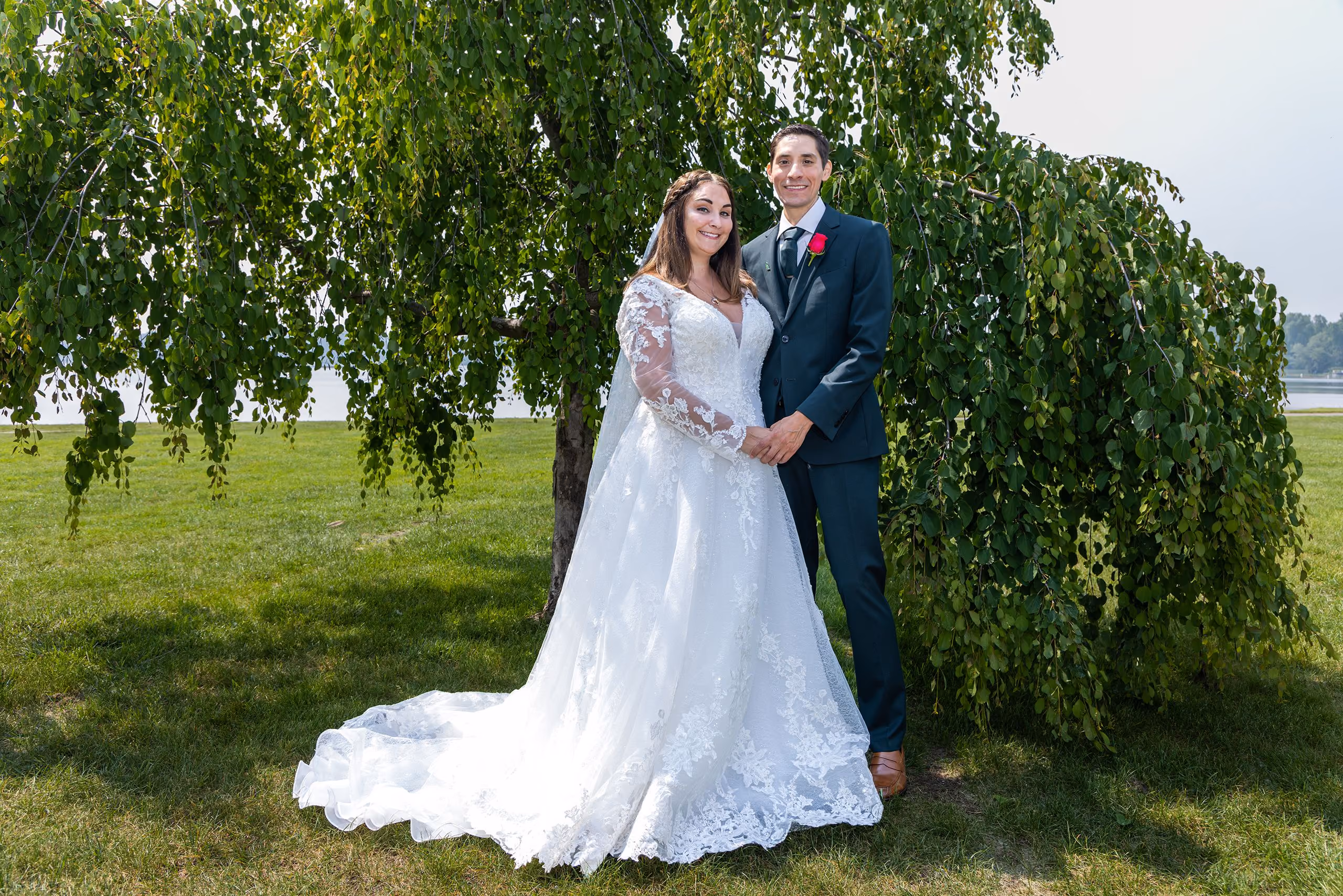 Newlywed couple beneath a willow tree near the water