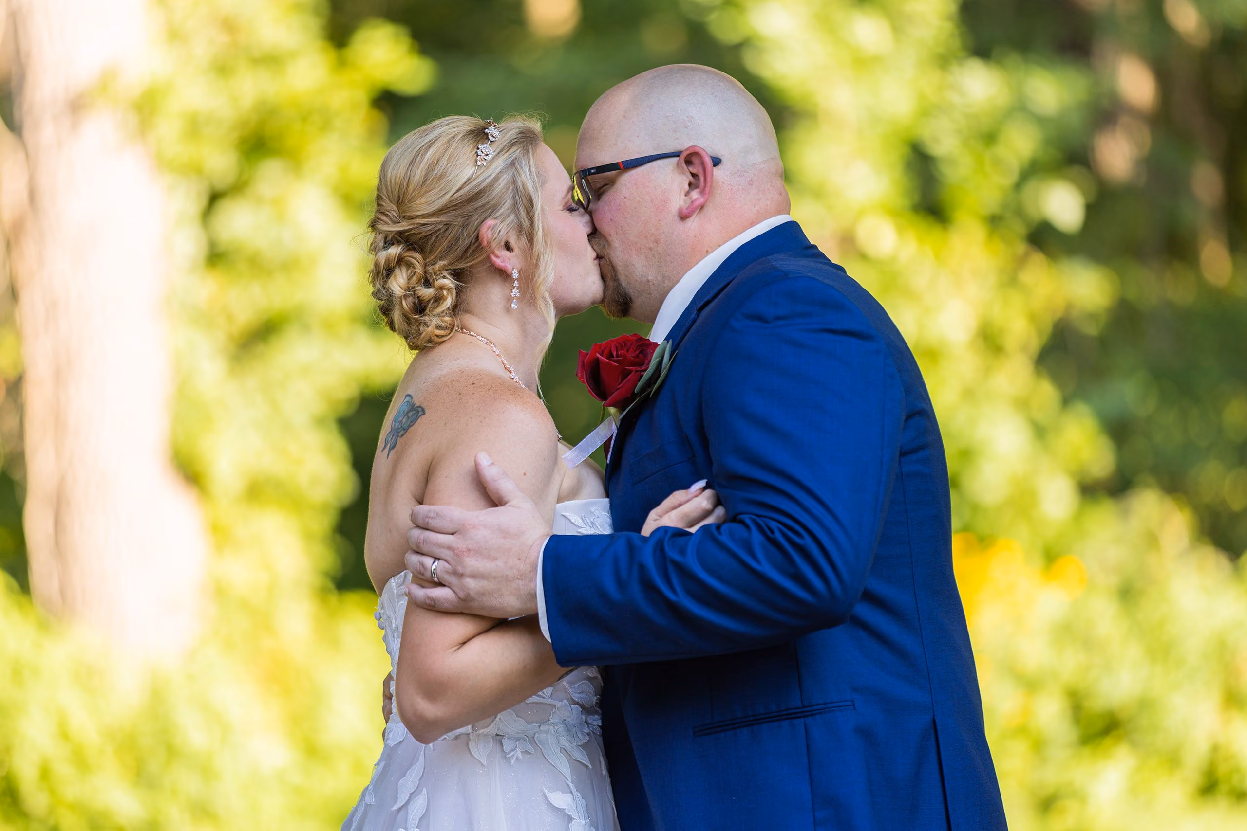 Bride and groom sharing a kiss surrounded by sunlit green foliage, Southeast Michigan wedding photographer