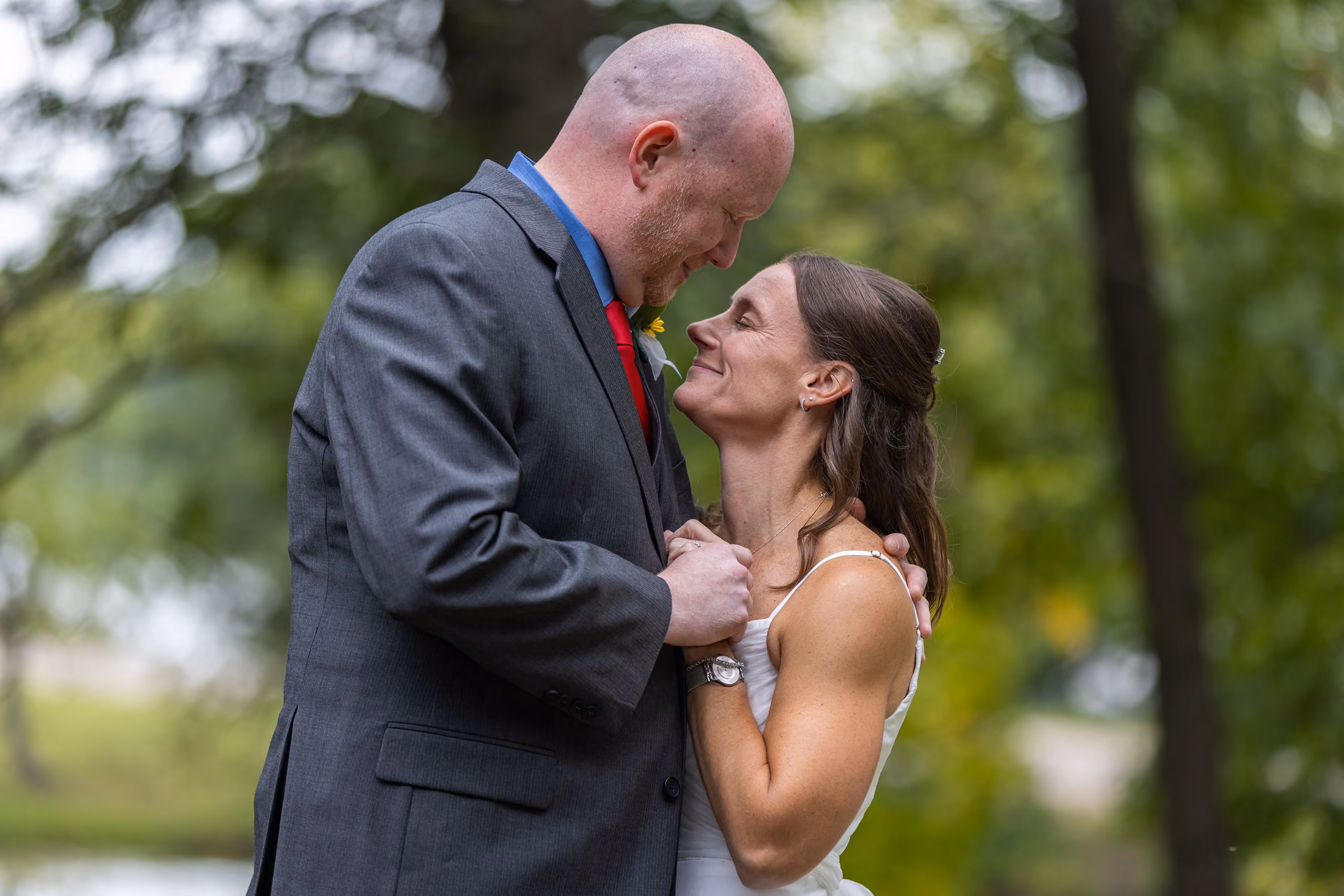 Bride and groom gazing at each other closely, surrounded by green trees, Milford Michigan wedding photographer