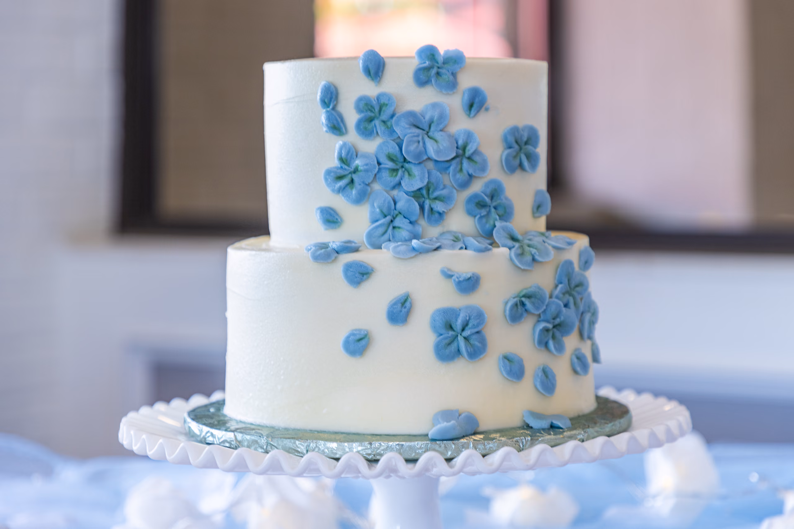 Two-tier white wedding cake decorated with blue sugar flowers cascading down the sides