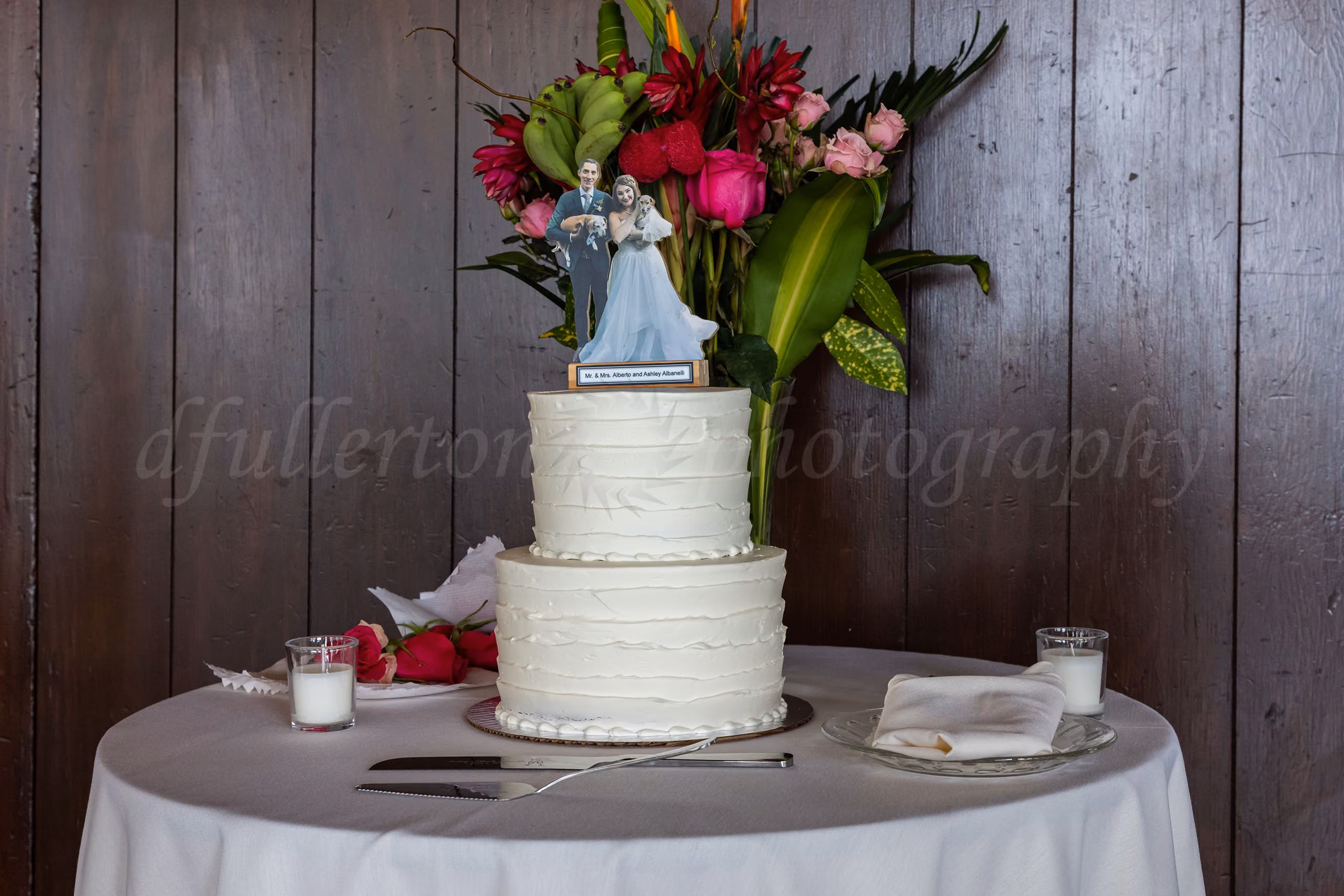 Two-tier white wedding cake with a personalized topper and tropical floral arrangement, wedding photography by Fullerton Photography