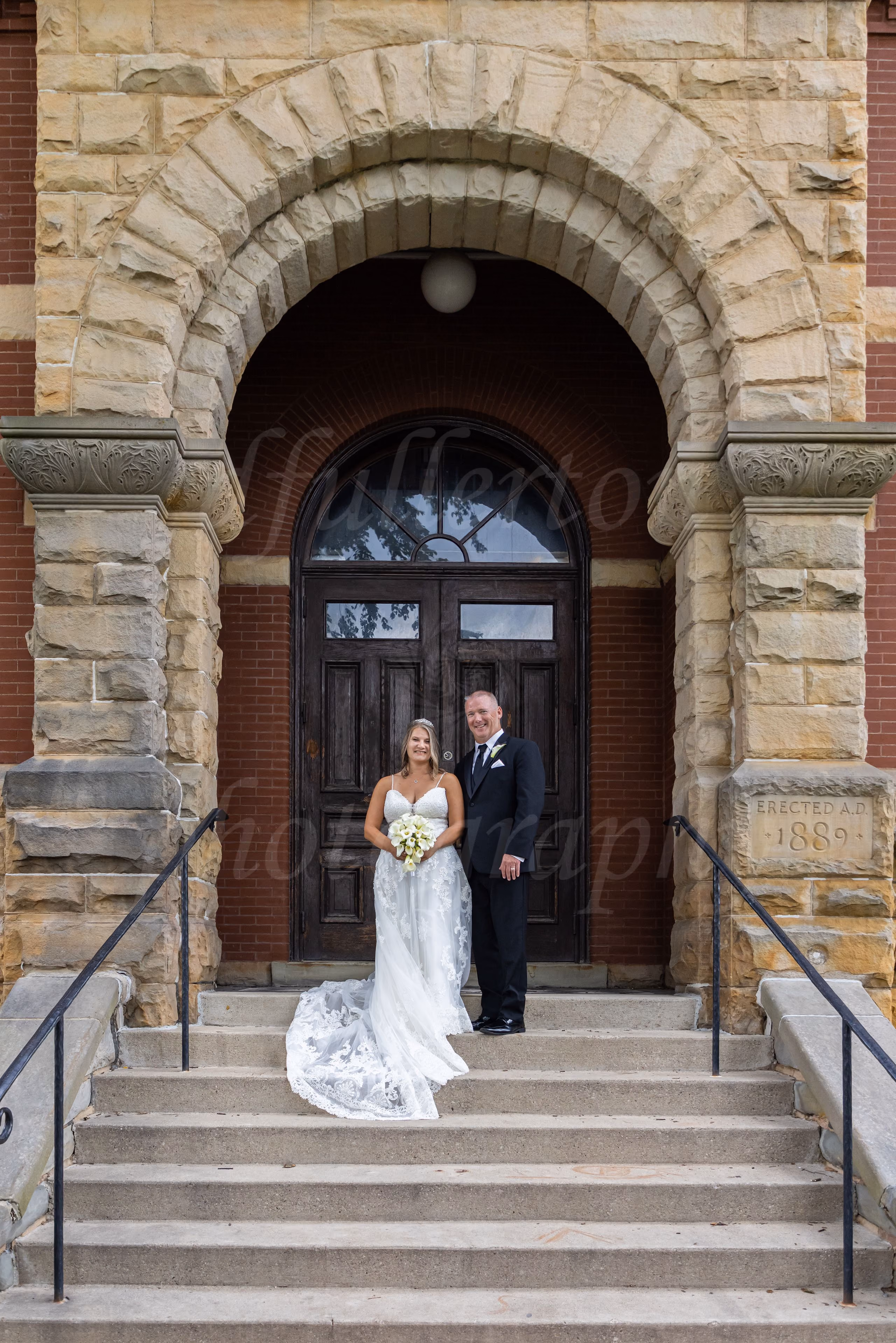 Bride and groom standing under a historic stone archway entrance dated 1889 in downtown Howell, MI