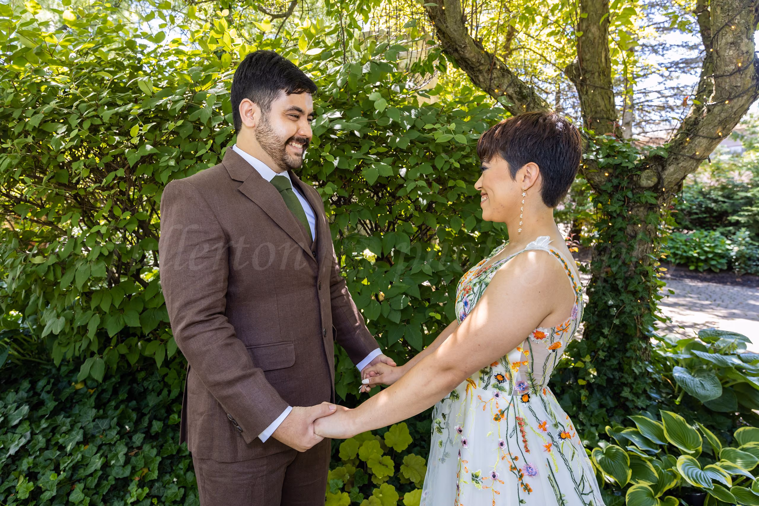 Groom in a brown suit holding hands with his bride in a colorful floral-embroidered gown in a garden