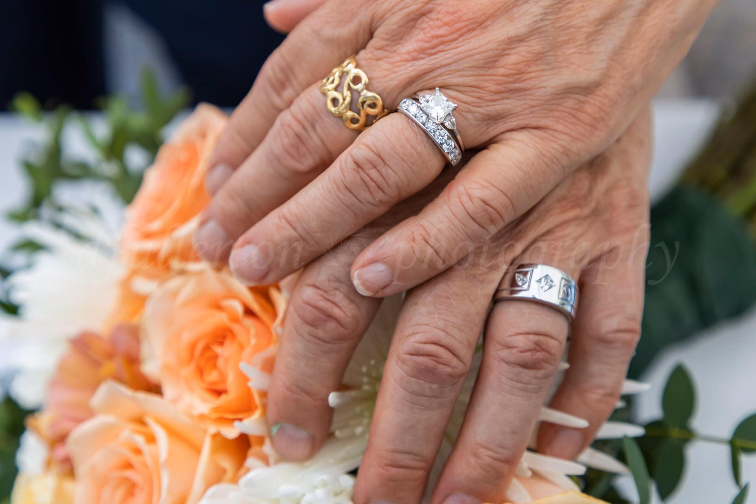 Close-up of wedding rings on bride and groom's hands resting on a peach rose bouquet