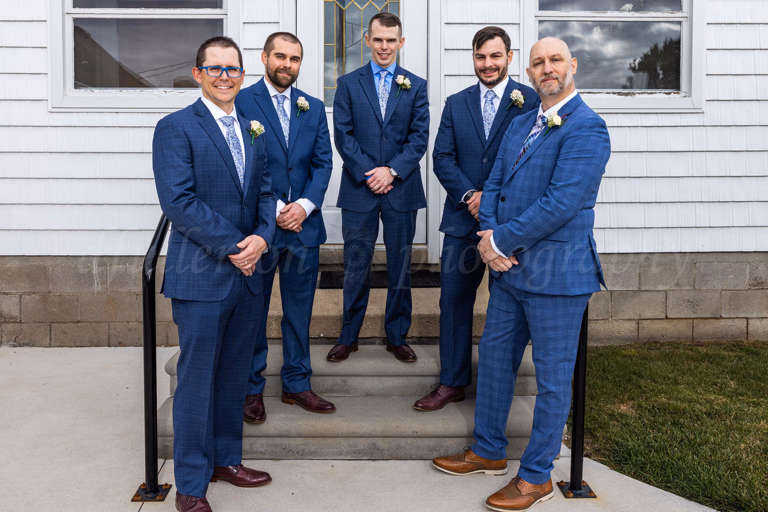 Groom and groomsmen in matching navy suits posing on steps outside a white church building