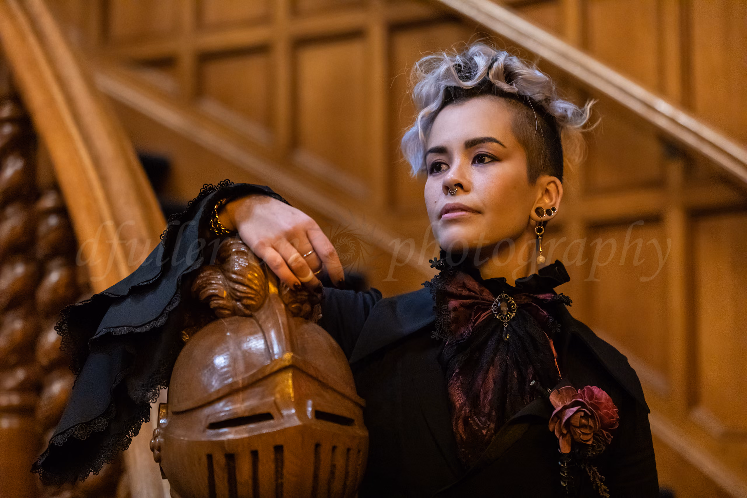Woman in gothic-style black attire posing beside a carved wooden knight's helmet banister