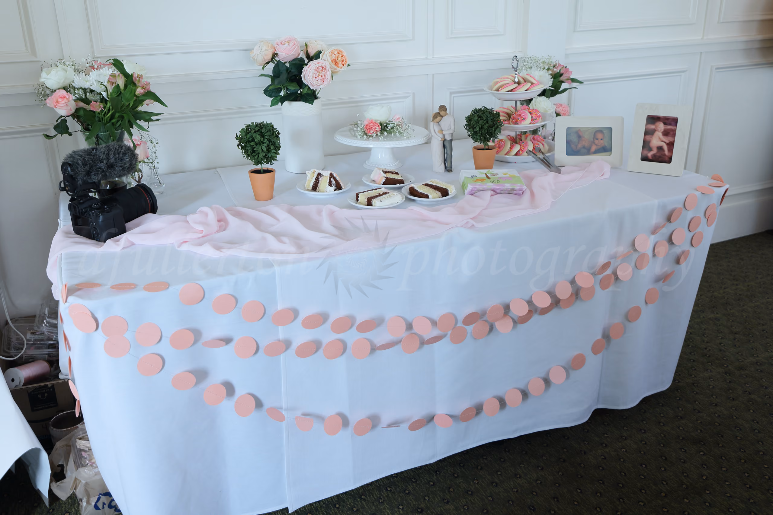 Baby shower dessert table decorated with pink garland, flowers, cake slices, and framed baby photos