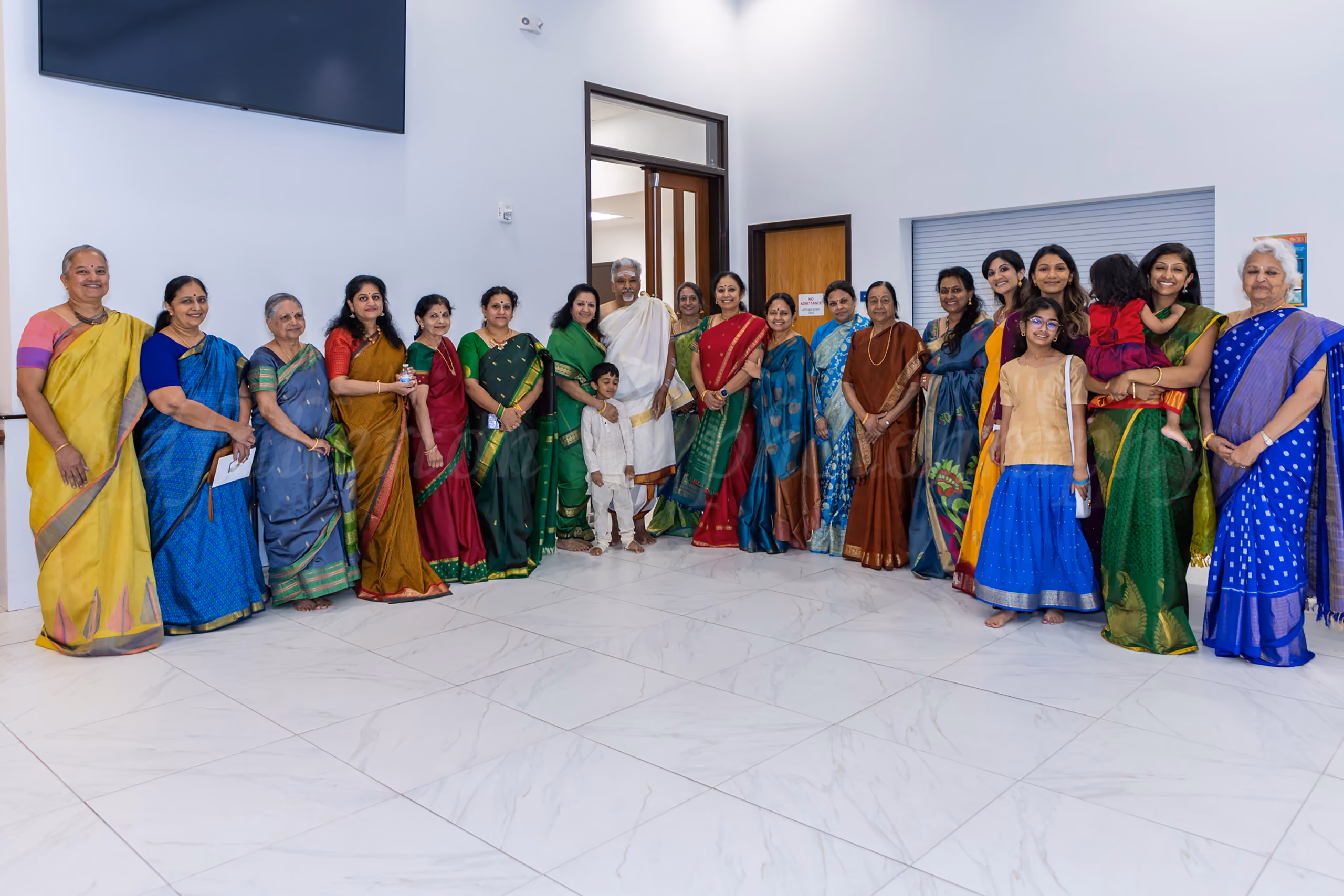Large family group photo in colorful traditional Indian saris and attire at a temple event