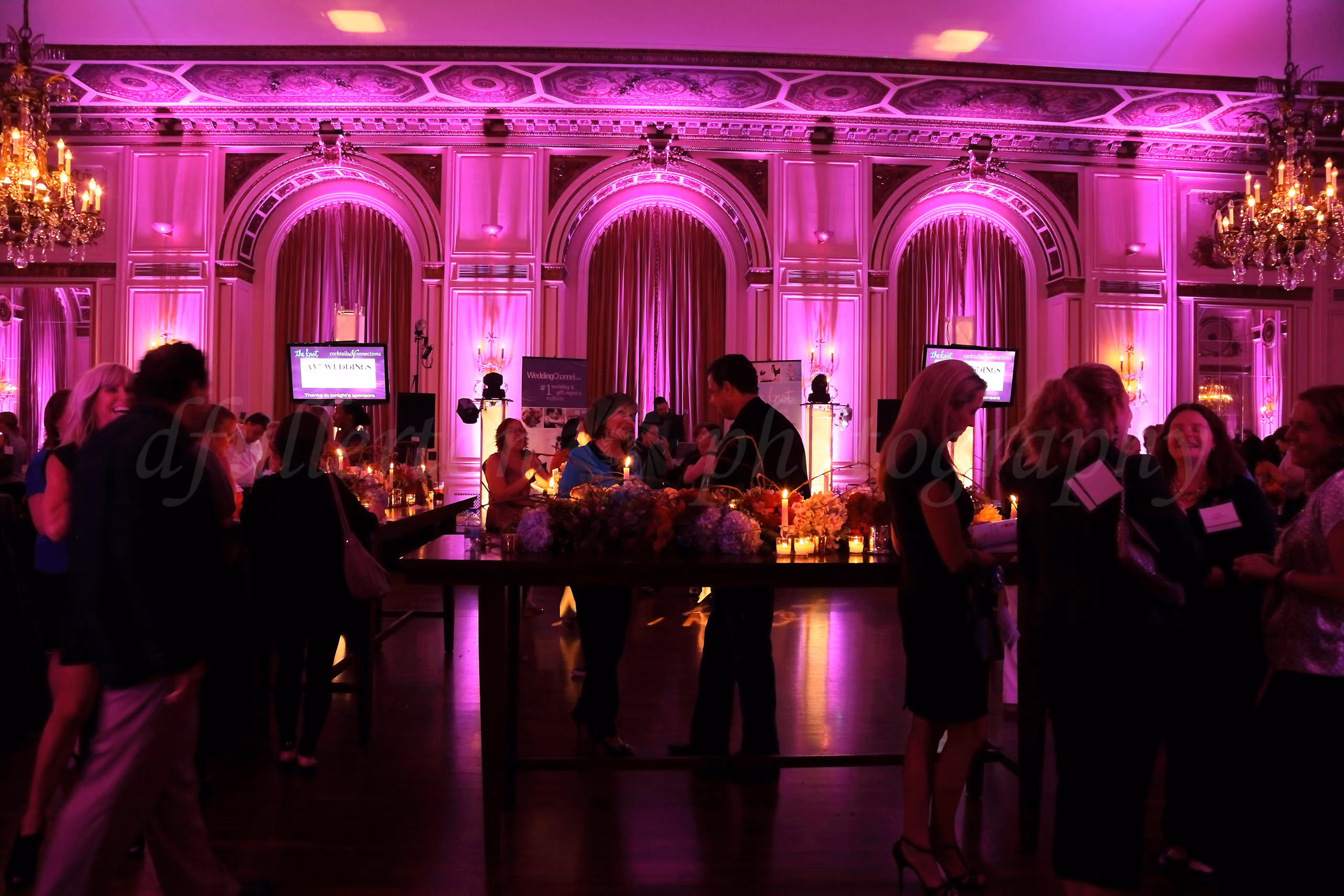 Guests mingling at a wedding industry networking event in an ornate ballroom lit with pink uplighting