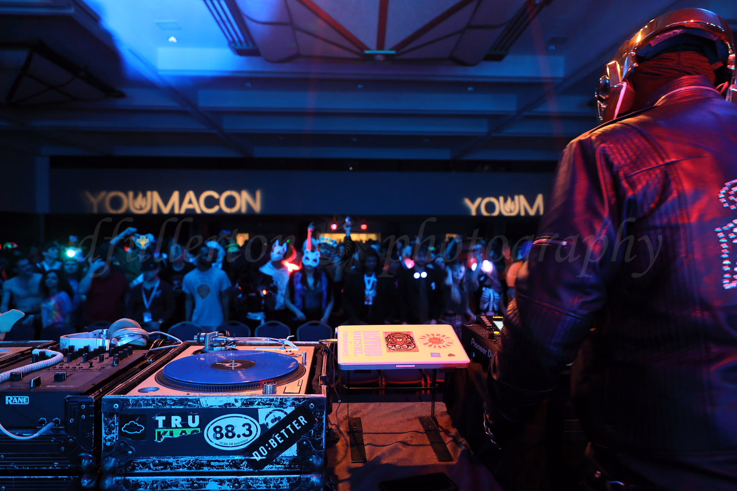DJ in a metallic helmet performing on turntables for a costumed crowd at the Youmacon convention