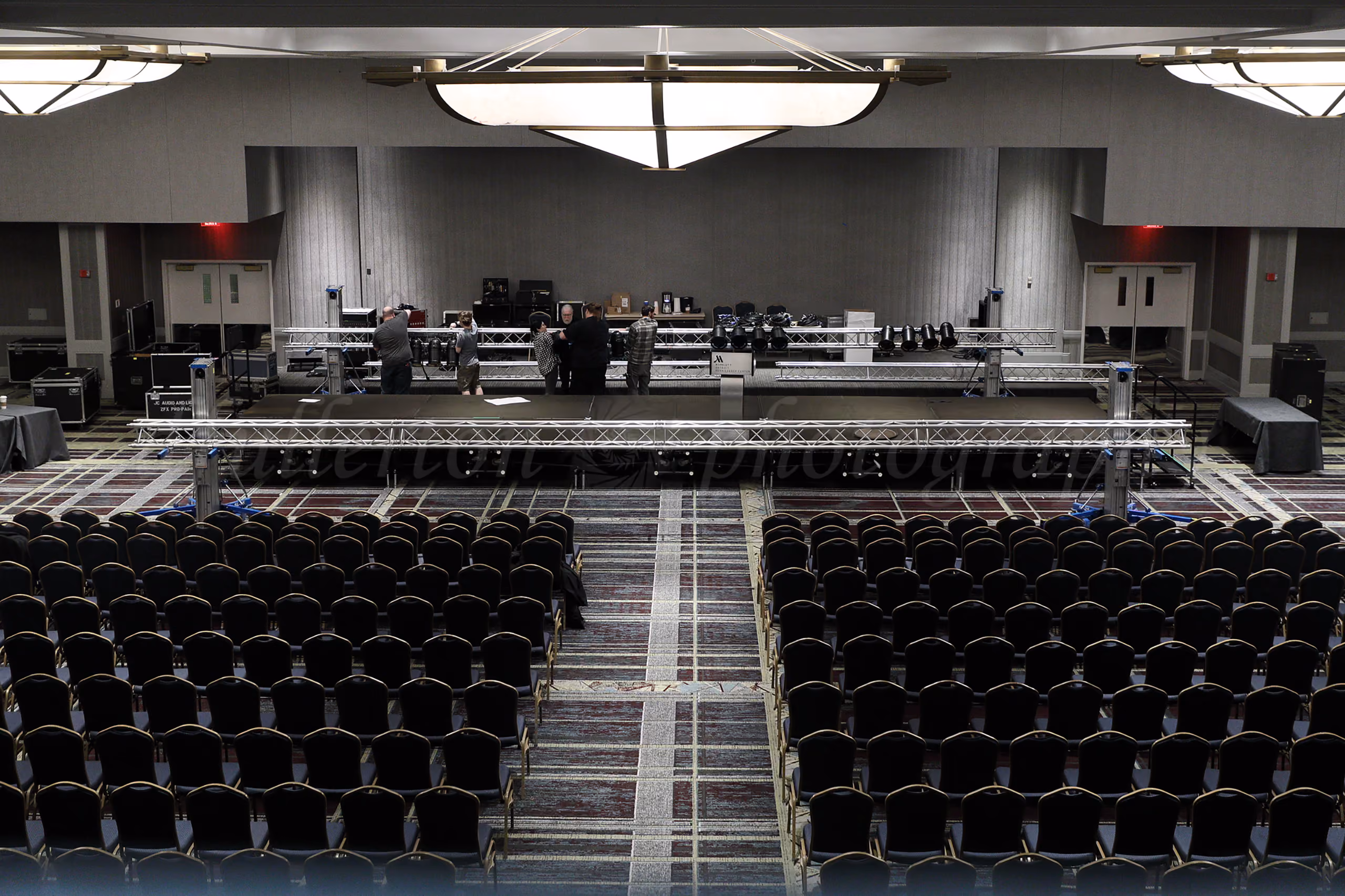 Event crew setting up sound and lighting equipment before an event in a large conference ballroom with rows of chairs
