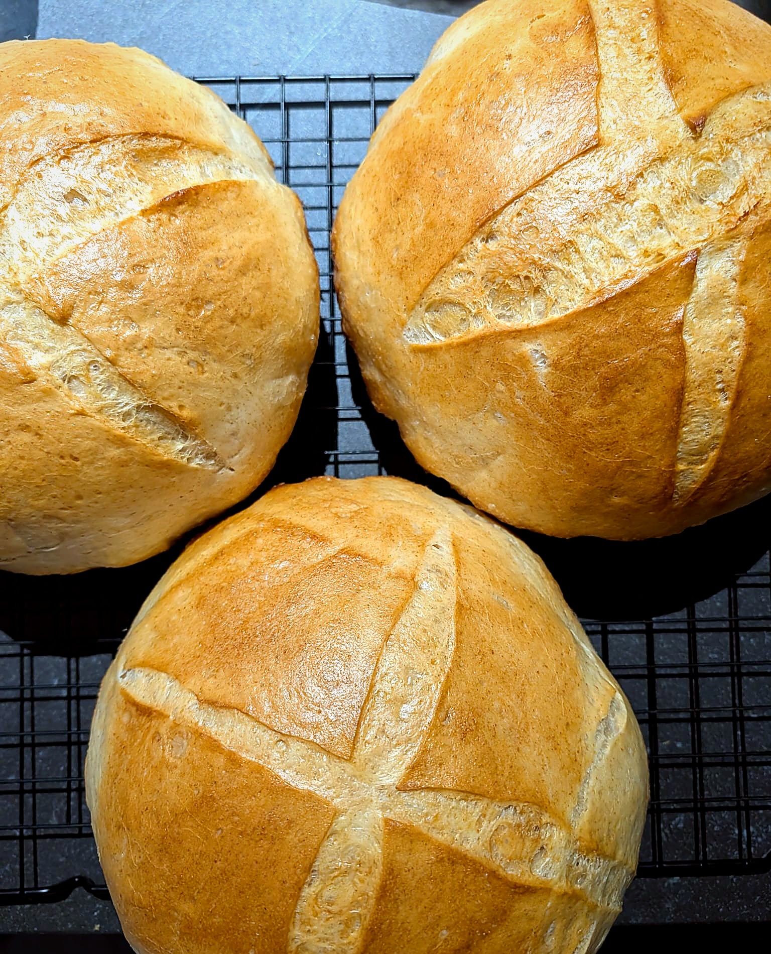 Three fresh sourdough loaves cooling, scored with an X