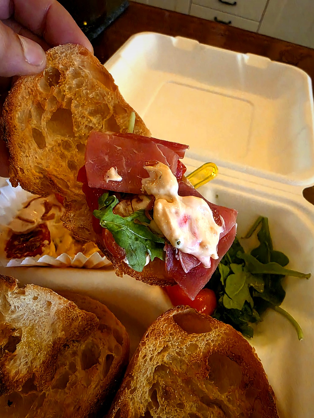 Hand-built open-face bite of sourdough, prosciutto, arugula and aioli
