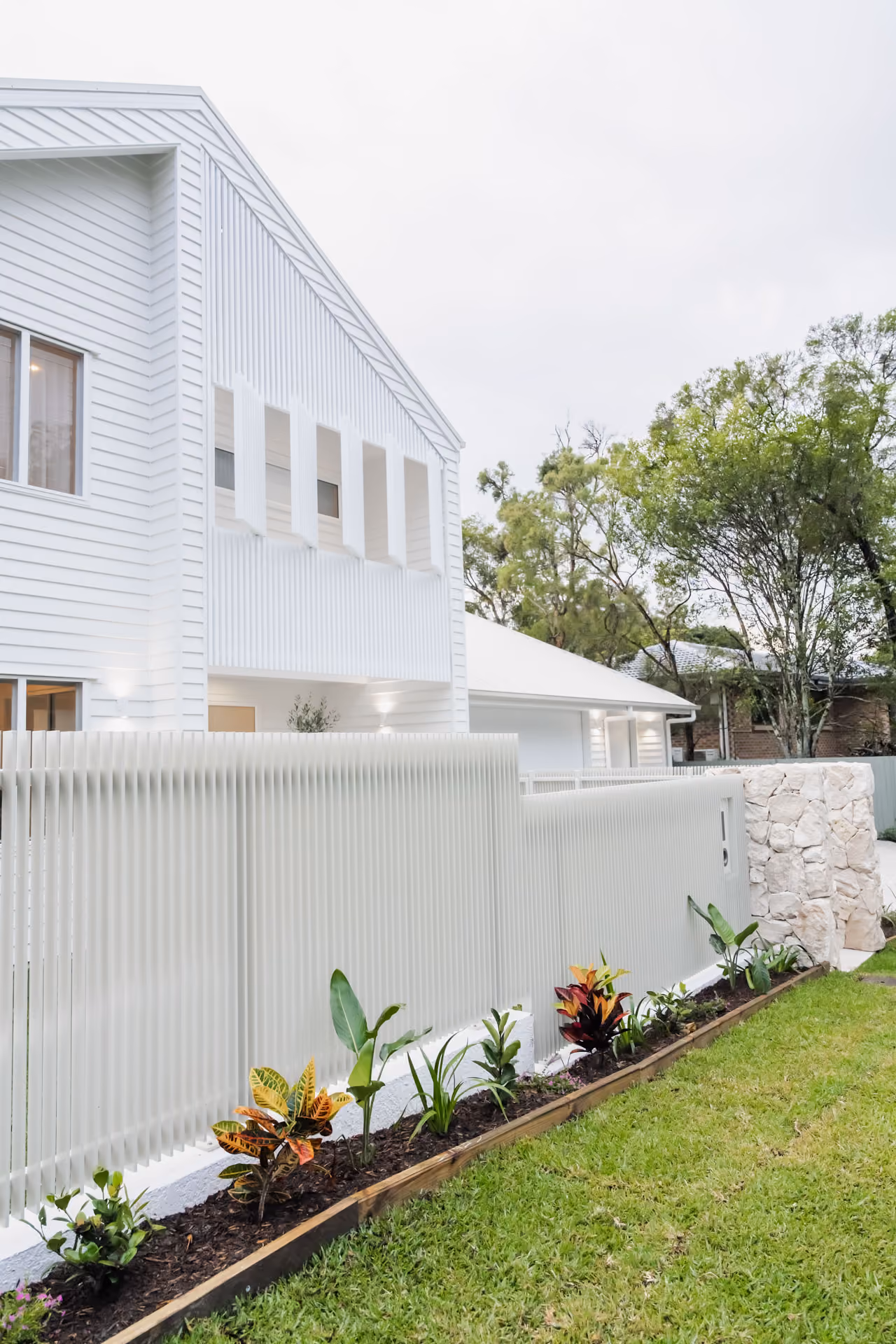 White weatherboard home behind a batten fence on an established block