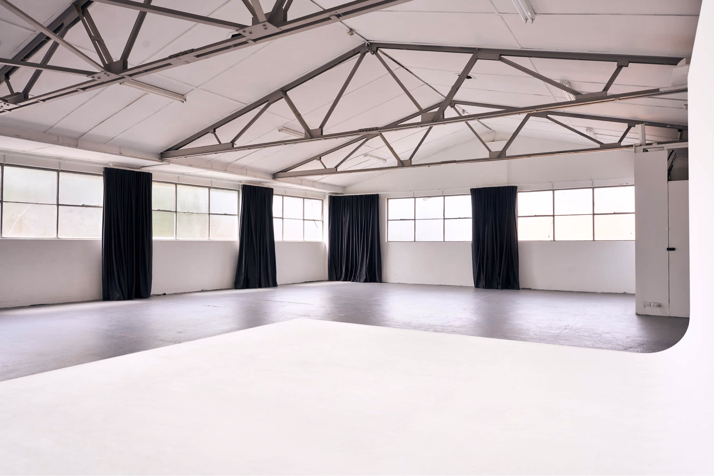 Frank the studio in daylight with the curtains pulled open. Industrial beams of the ceiling are visible in the clean rustic studio