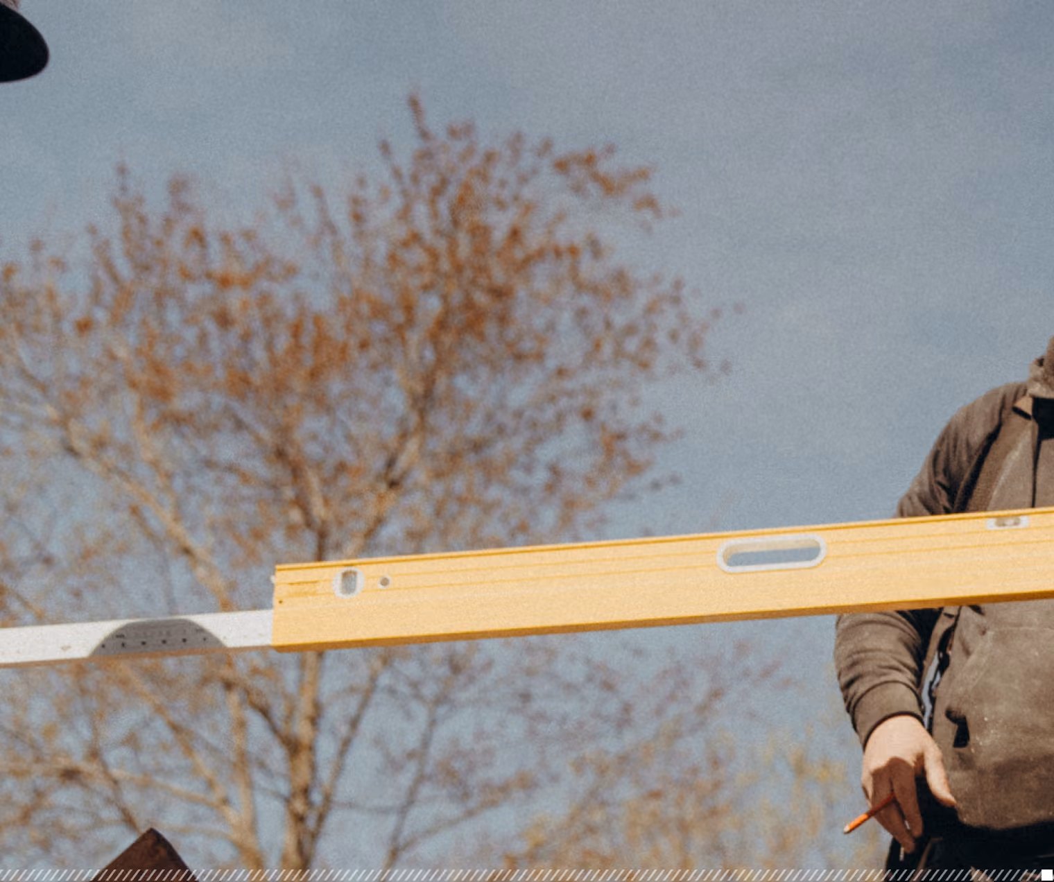 Person holding a yellow spirit level outdoors with trees and a clear sky in the background.