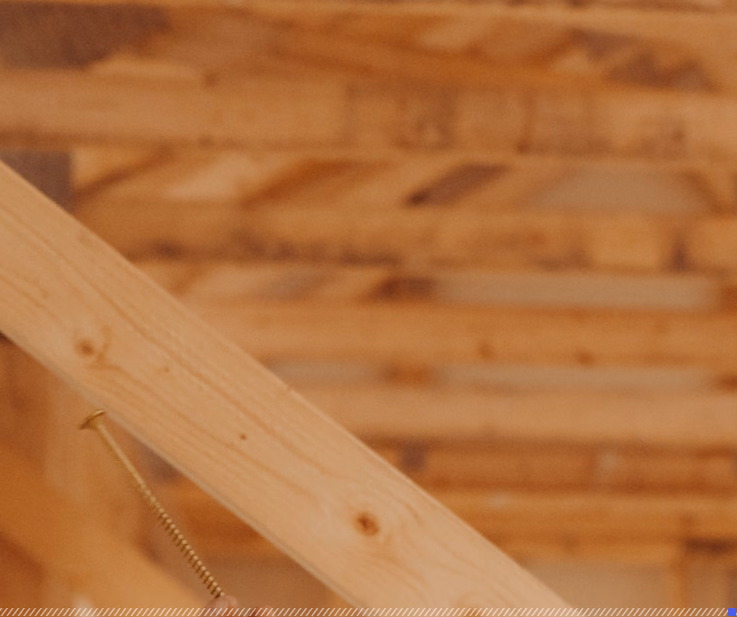 Close-up of a wooden beam with a large, partially inserted screw in a construction setting with blurred wooden framework background.