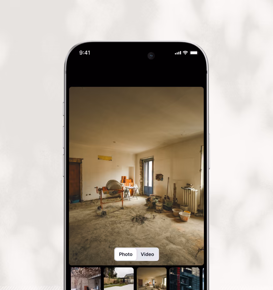 Smartphone screen showing a construction site with a cement mixer, buckets, and construction materials in a room with dusty floor and a door leading outside.