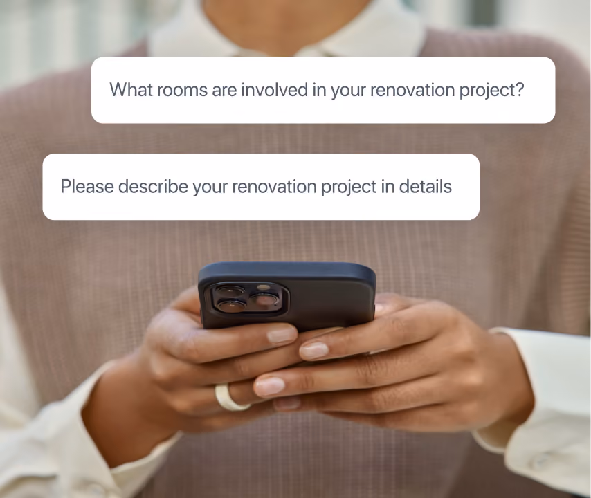 Close-up of a person holding a smartphone with two text messages on screen: 'What rooms are involved in your renovation project?' and 'Please describe your renovation project in details.'