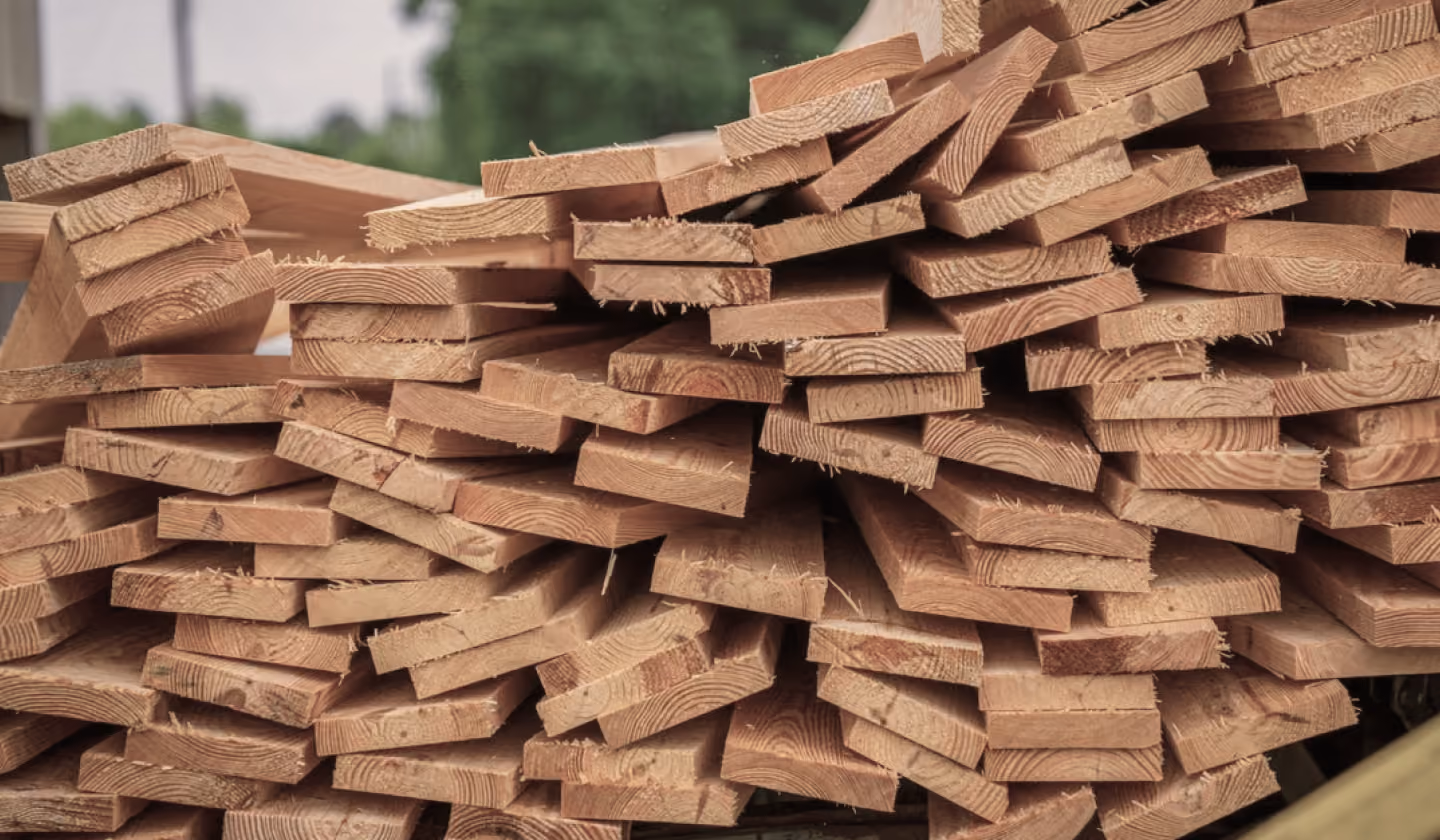 Stack of rough-cut wooden planks piled for construction or woodworking.