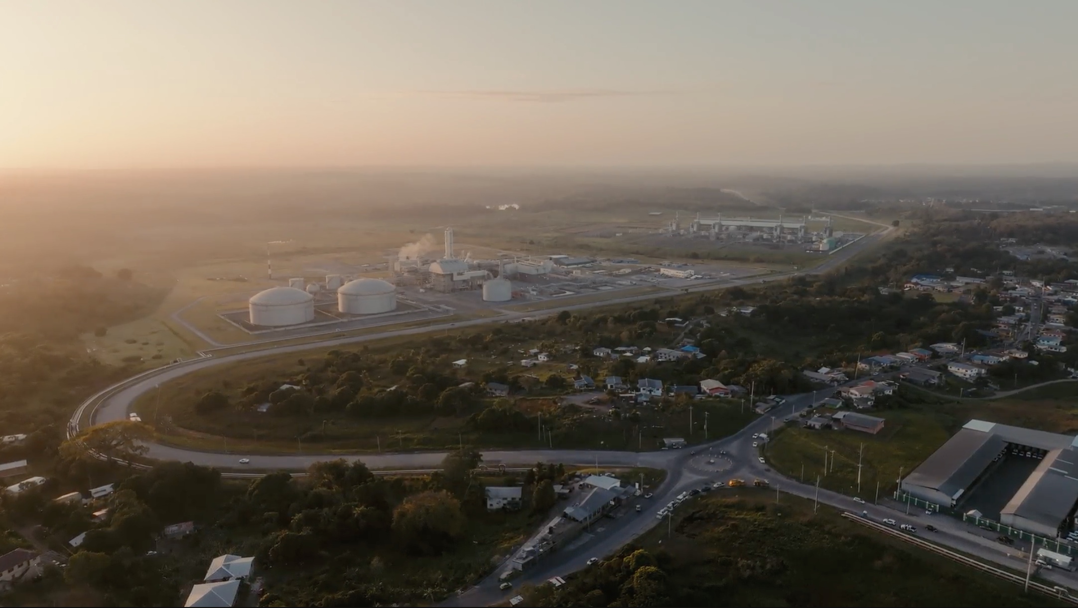 Aerial view at sunset of Trinidad's industrial coastline, with storage tanks and a processing plant set among towns and roads