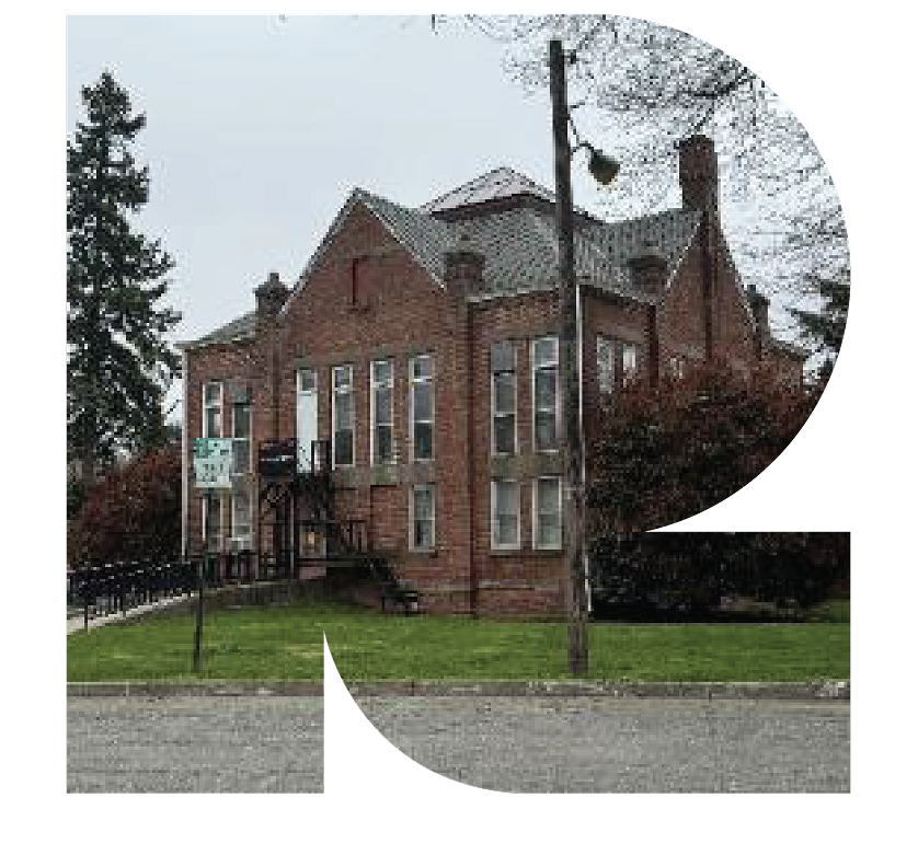 Two-story brick building with many windows, green lawn, and a streetlamp in front on a cloudy day.