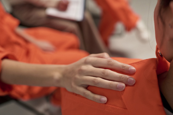 A supportive hand resting on the shoulder of a person in an orange jumpsuit, representing Hometown Health System correctional care.