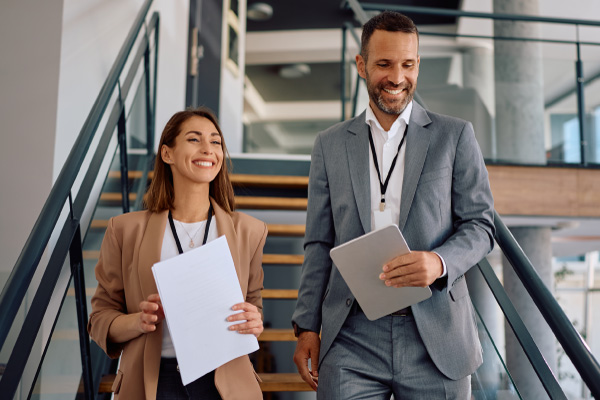 Two smiling healthcare executives walking down stairs with documents and a tablet, highlighting Hometown Health System retail pharmacy partners.