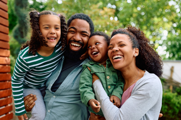 A joyful Black family of four laughing together outdoors, representing Hometown Health System care for patients and families.