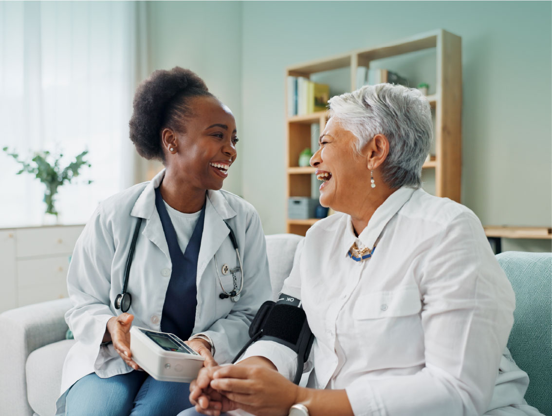 A smiling Black female healthcare professional sharing a warm, joyful moment with a senior patient in a bright medical setting.