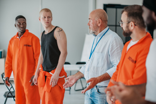 An instructor facilitating a group support session with individuals in orange correctional jumpsuits, representing Hometown Health System's whole-person care.