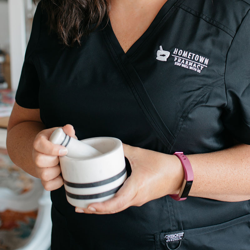 A Hometown Health System pharmacist in branded black scrubs holding a ceramic mortar and pestle.