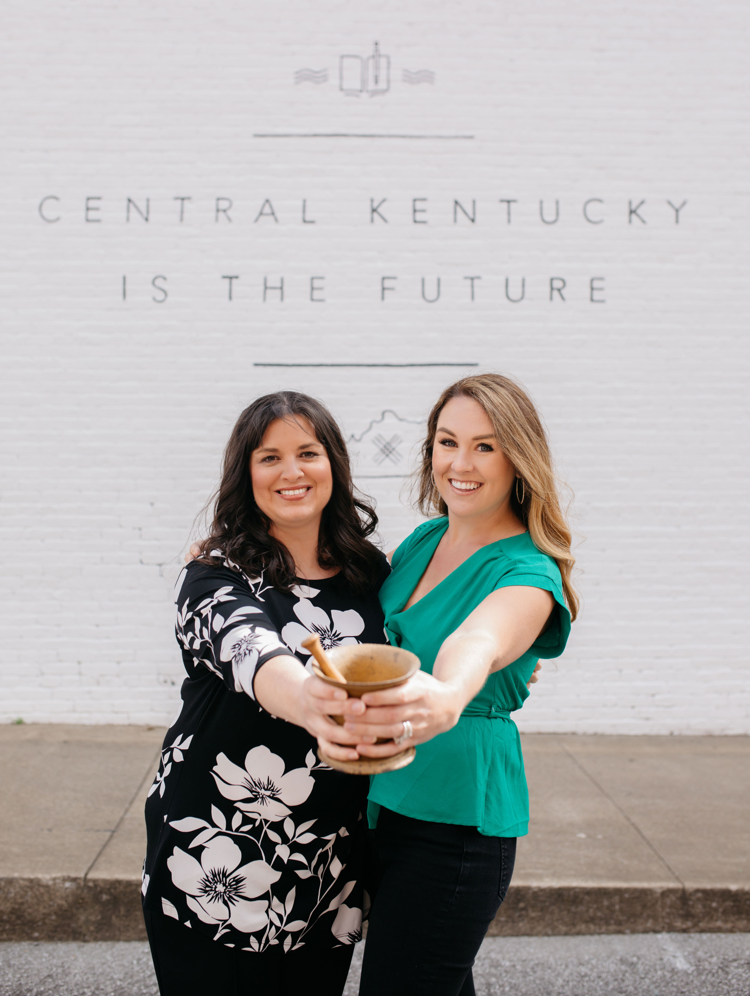 Two smiling Hometown Health System leaders holding a mortar and pestle in front of a white wall reading "Central Kentucky is the future."