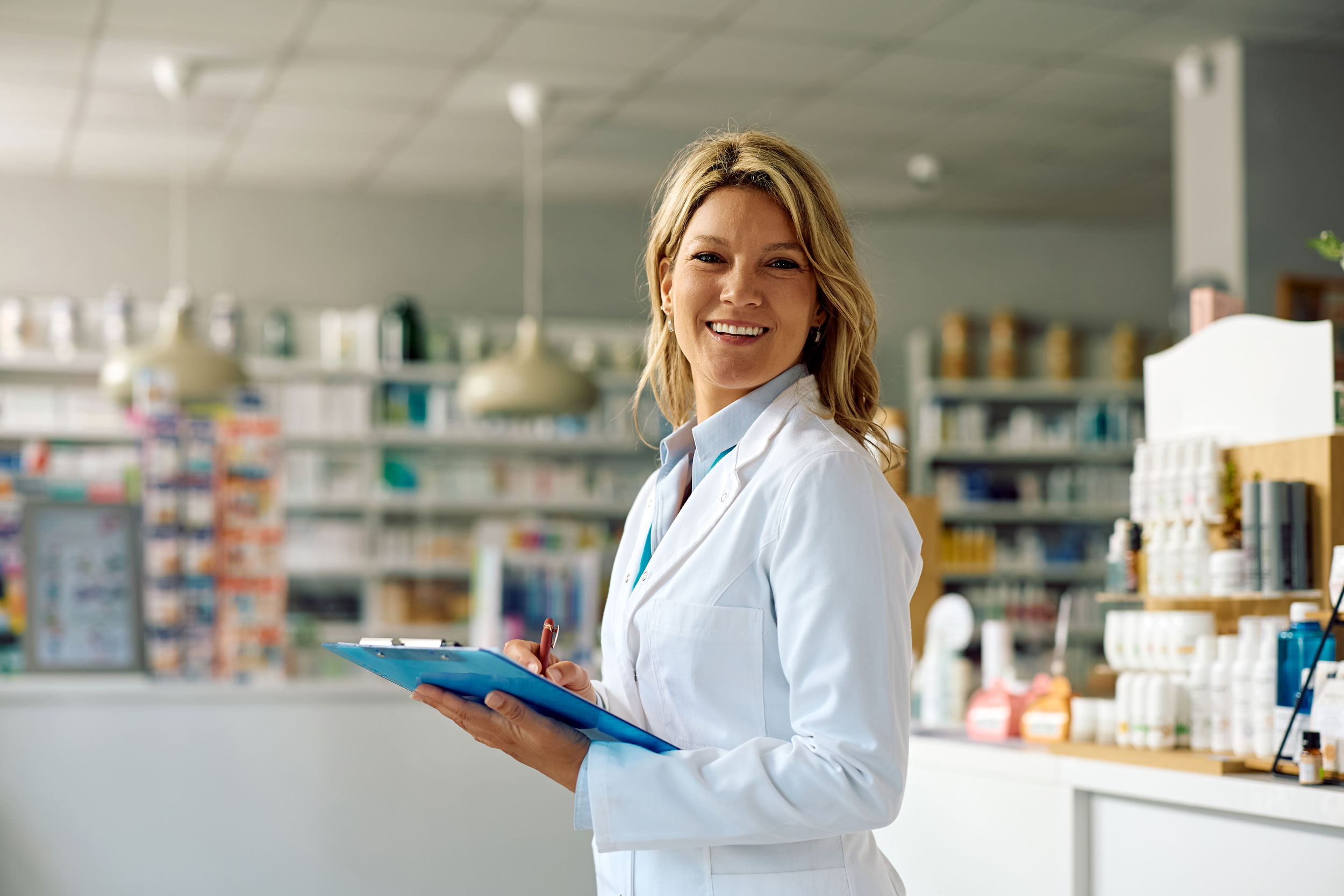 A smiling female pharmacist holding a clipboard, representing Hometown Health System's expanded retail pharmacy access.