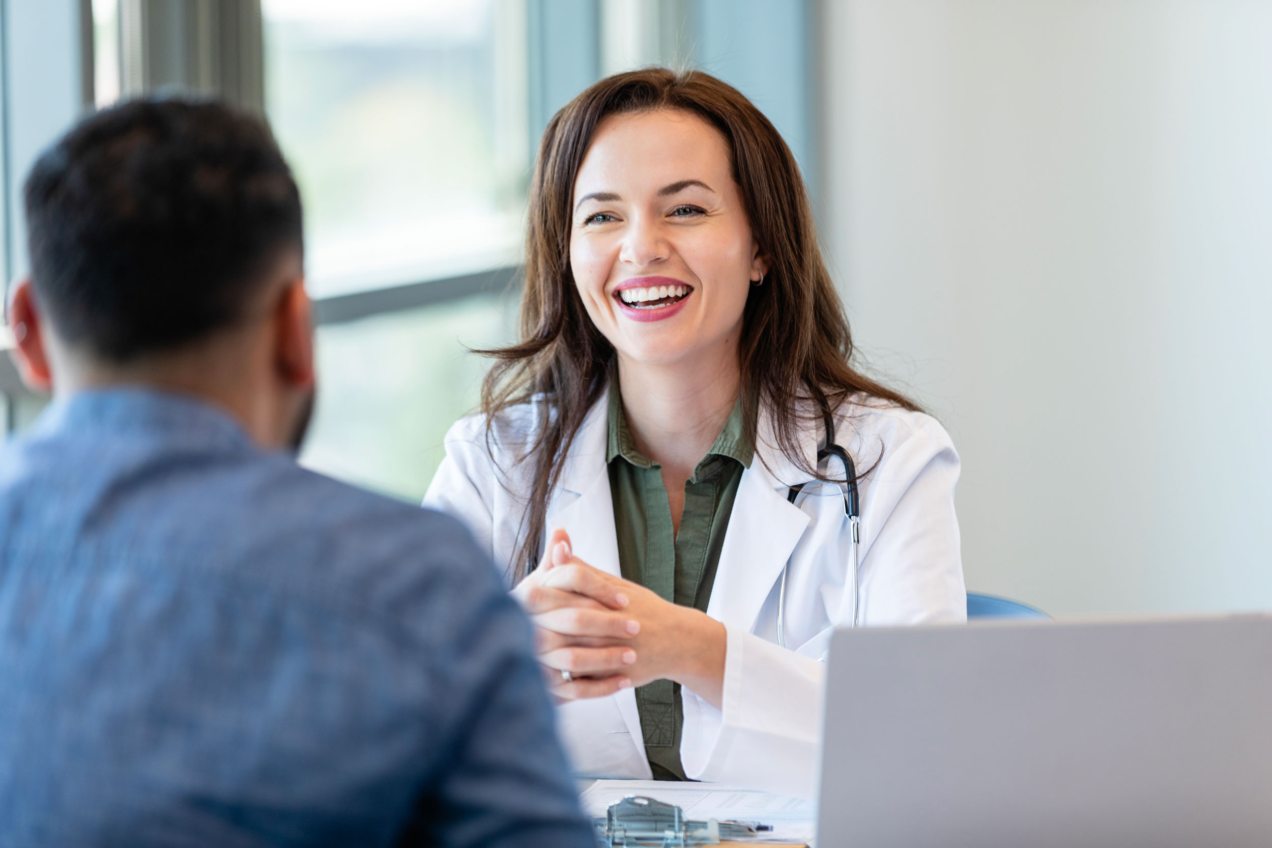 A smiling female doctor with a stethoscope sitting across from a patient, representing Hometown Health System's community connection program.
